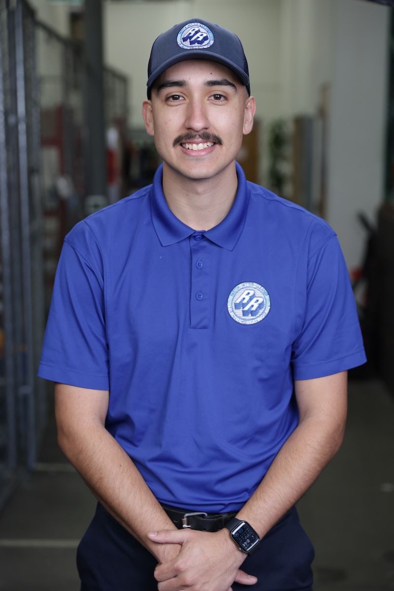 Man in a blue polo and cap standing indoors, smiling at the camera