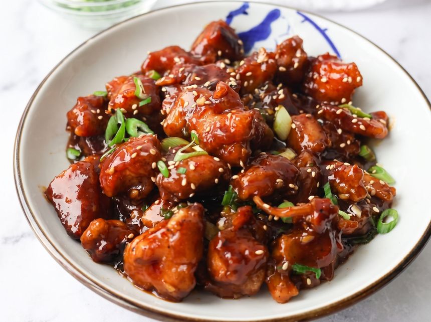 Glazed saucy chicken pieces garnished with green onions on a white plate