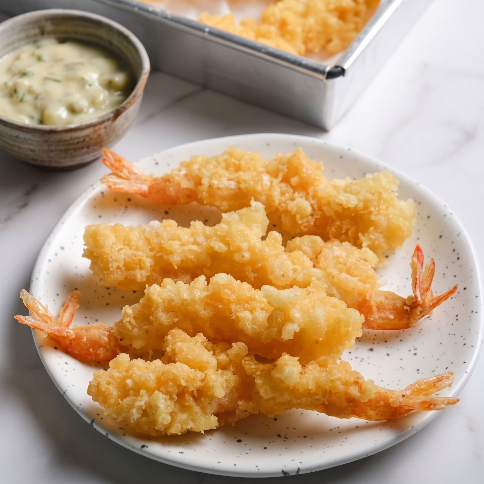 Plate of crispy tempura shrimp with dipping sauce on a white table