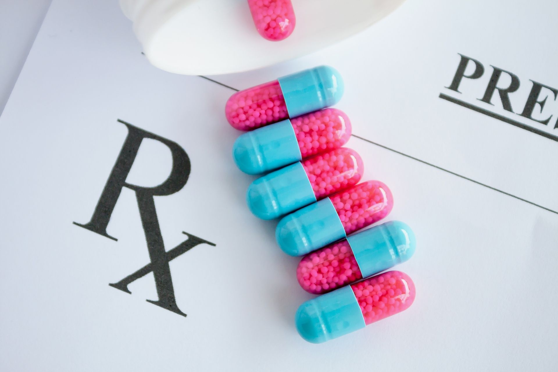 Image of pink and blue capsules spilling out of a pill bottle