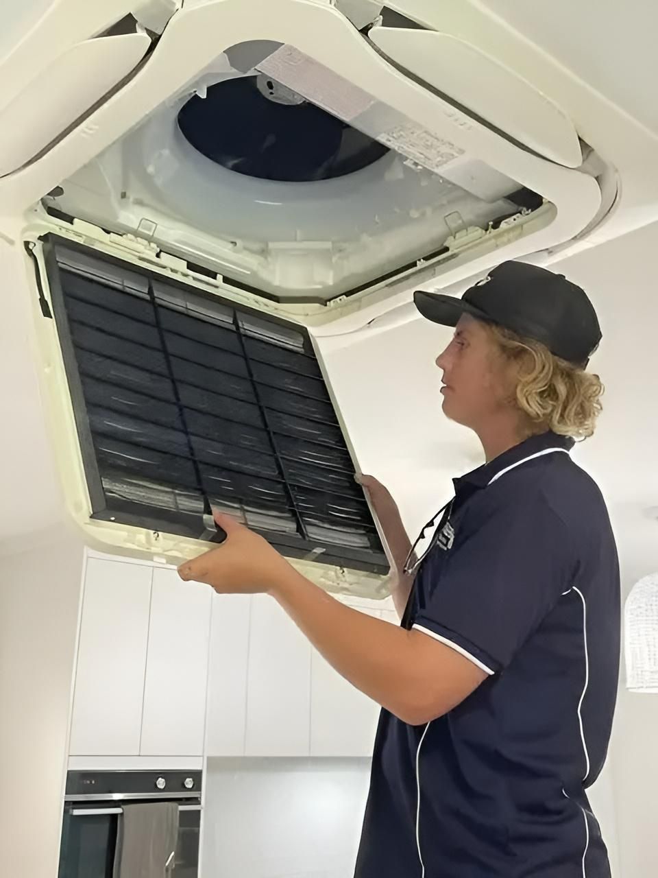 A Man Is Cleaning A Ceiling Fan With A Filter — Beards Refrigeration & Air Conditioning in Mackay, QLD