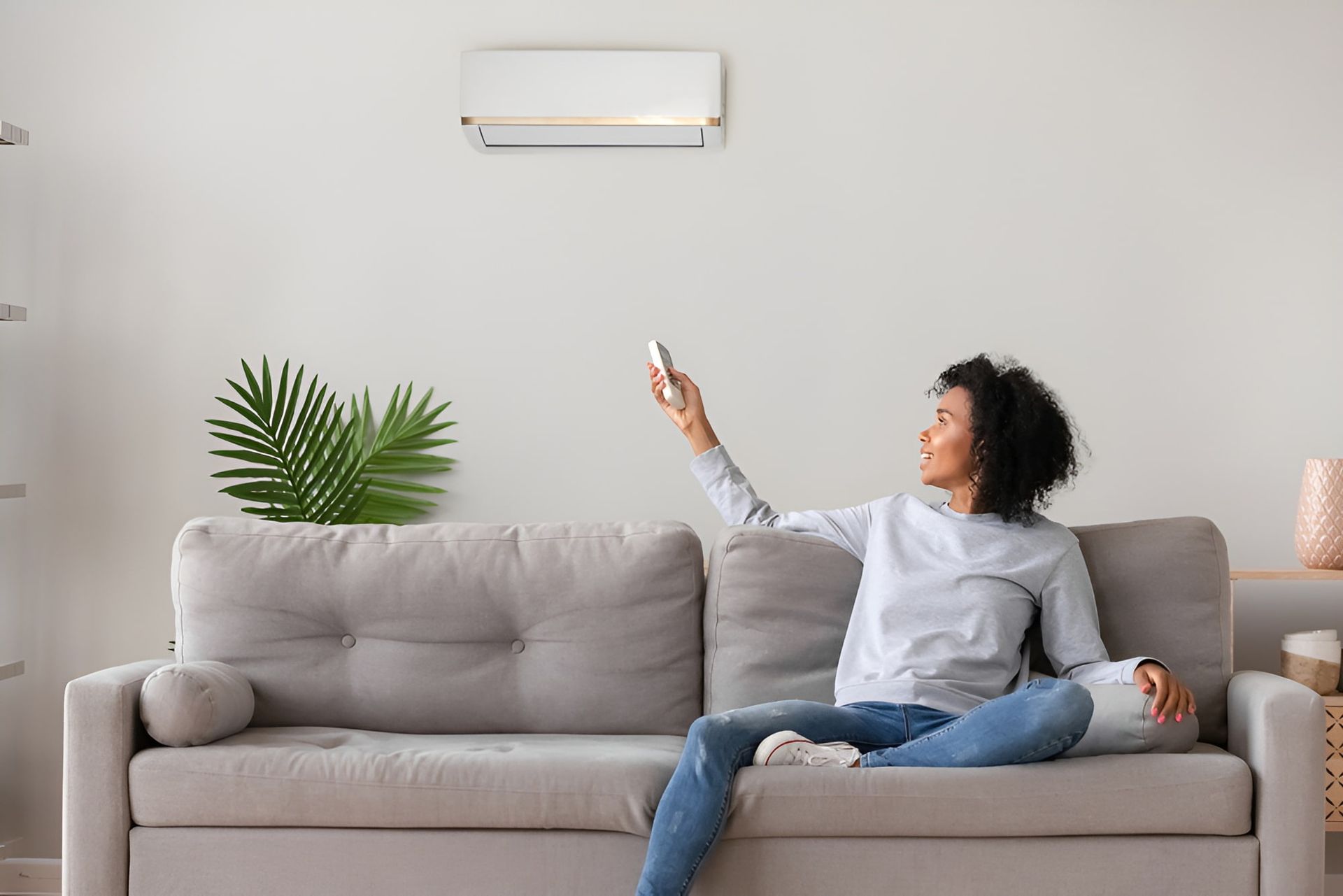 A Woman Is Sitting On A Couch Holding A Remote Control — Beards Refrigeration & Air Conditioning in Sarina, QLD