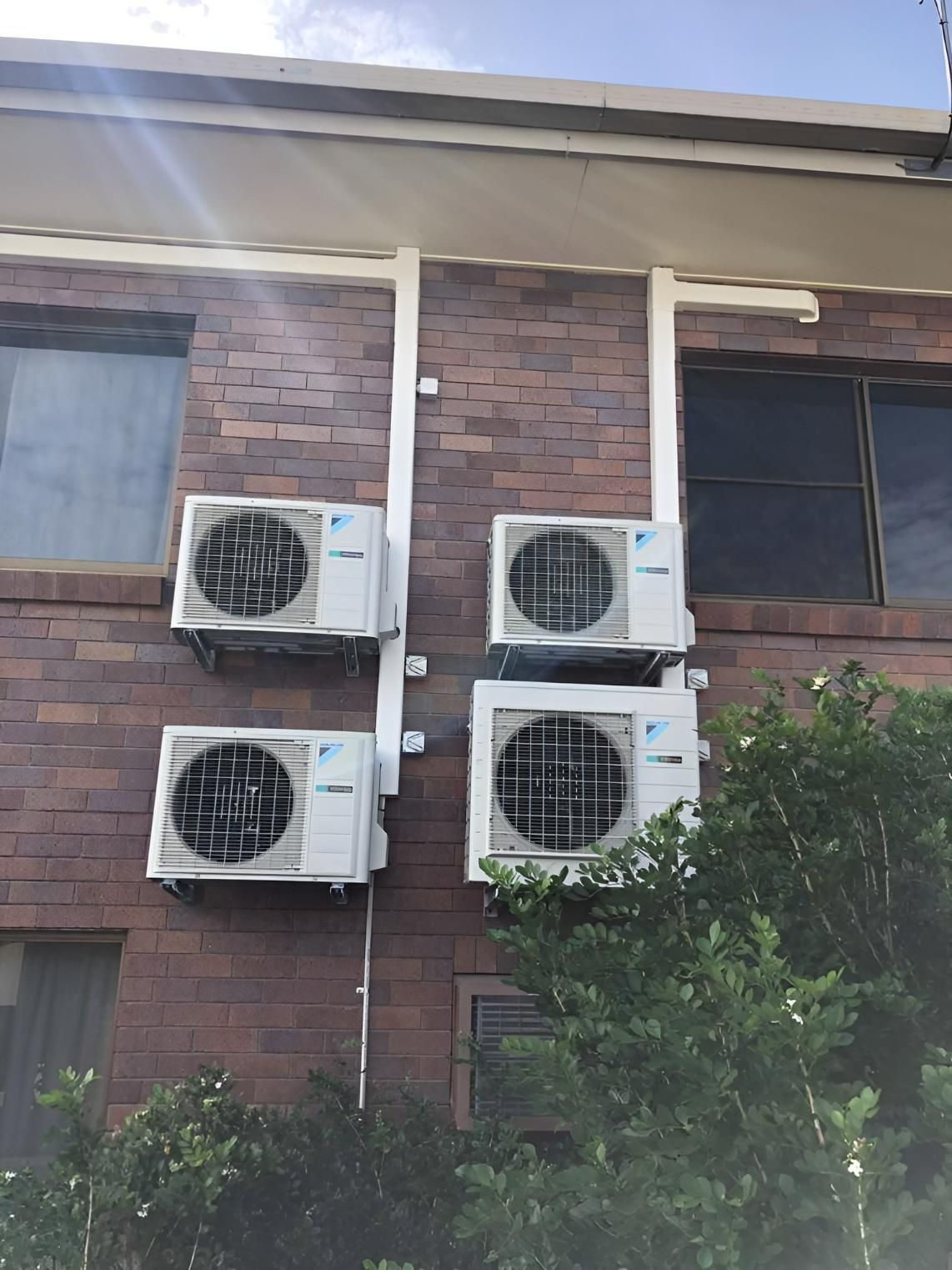 Four Air Conditioners Are Mounted On The Side Of A Brick Building — Beards Refrigeration & Air Conditioning in Bucasia, QLD