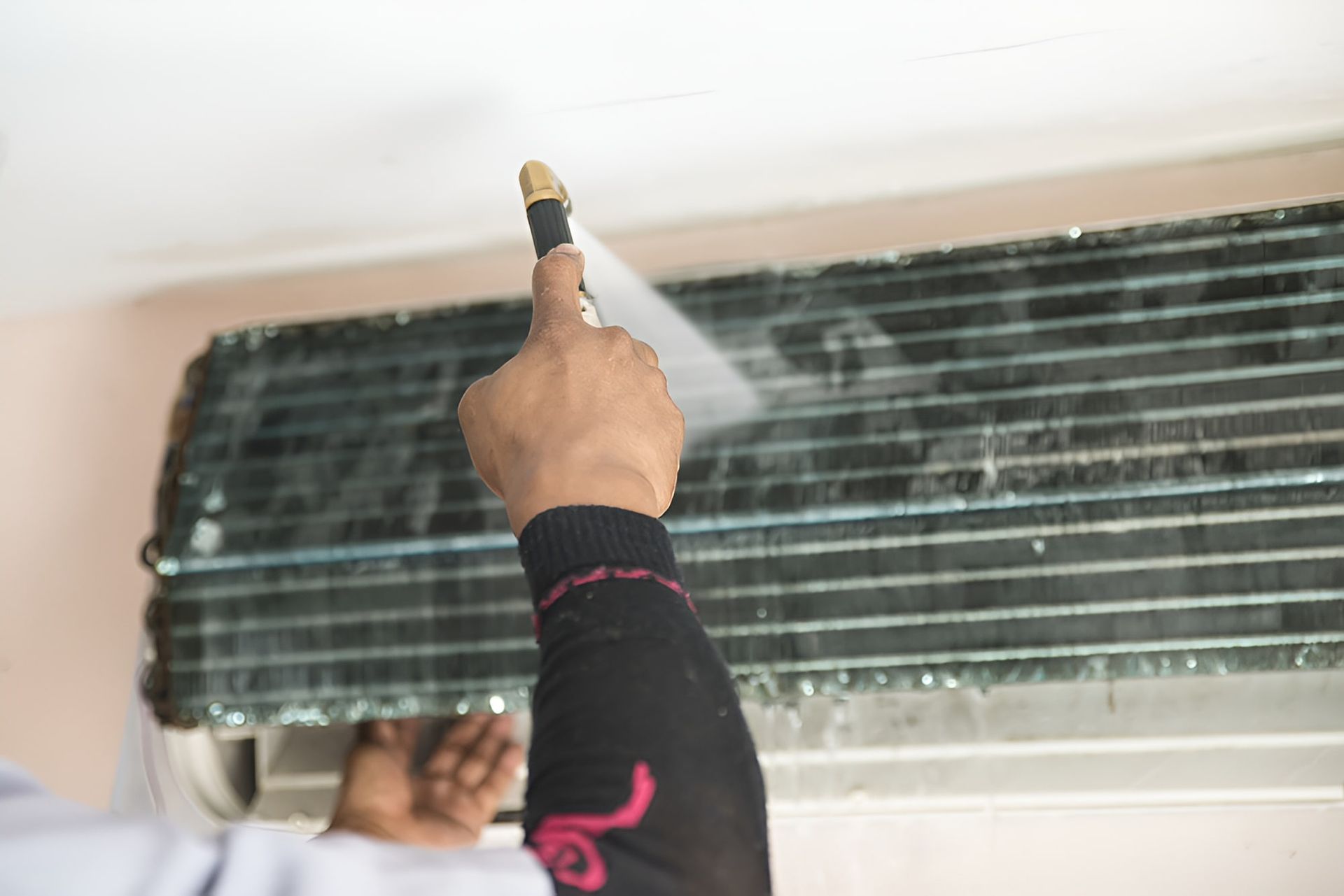 A Person Is Cleaning An Air Conditioner With A Spray Bottle — Beards Refrigeration & Air Conditioning in Rural View, QLD