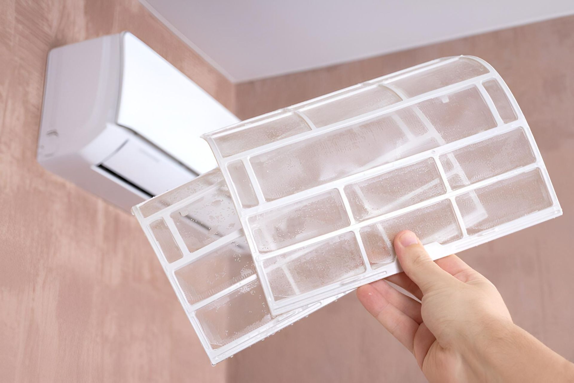 A Person Is Holding A Filter In Front Of An Air Conditioner — Beards Refrigeration & Air Conditioning in Mackay, QLD
