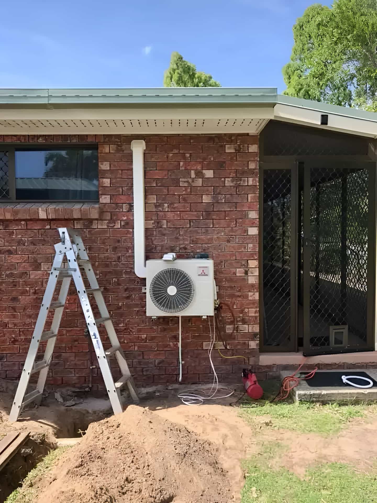 A Ladder Is Sitting In Front Of A Brick House With A Fan On The Side — Beards Refrigeration & Air Conditioning in Bucasia, QLD
