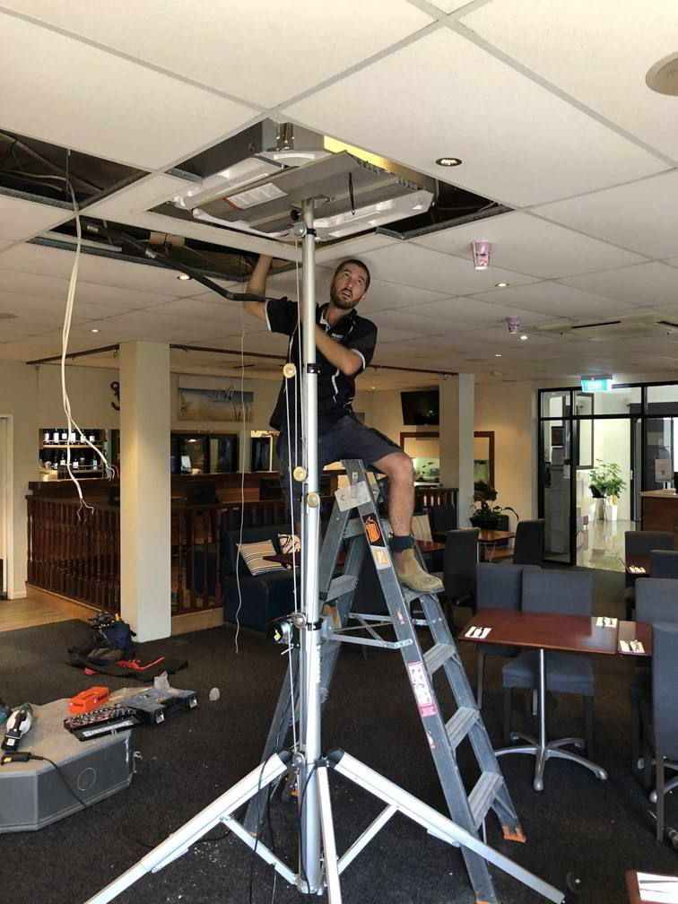 A Man On A Ladder Working On A Ceiling Fan — Beards Refrigeration & Air Conditioning in Sarina, QLD