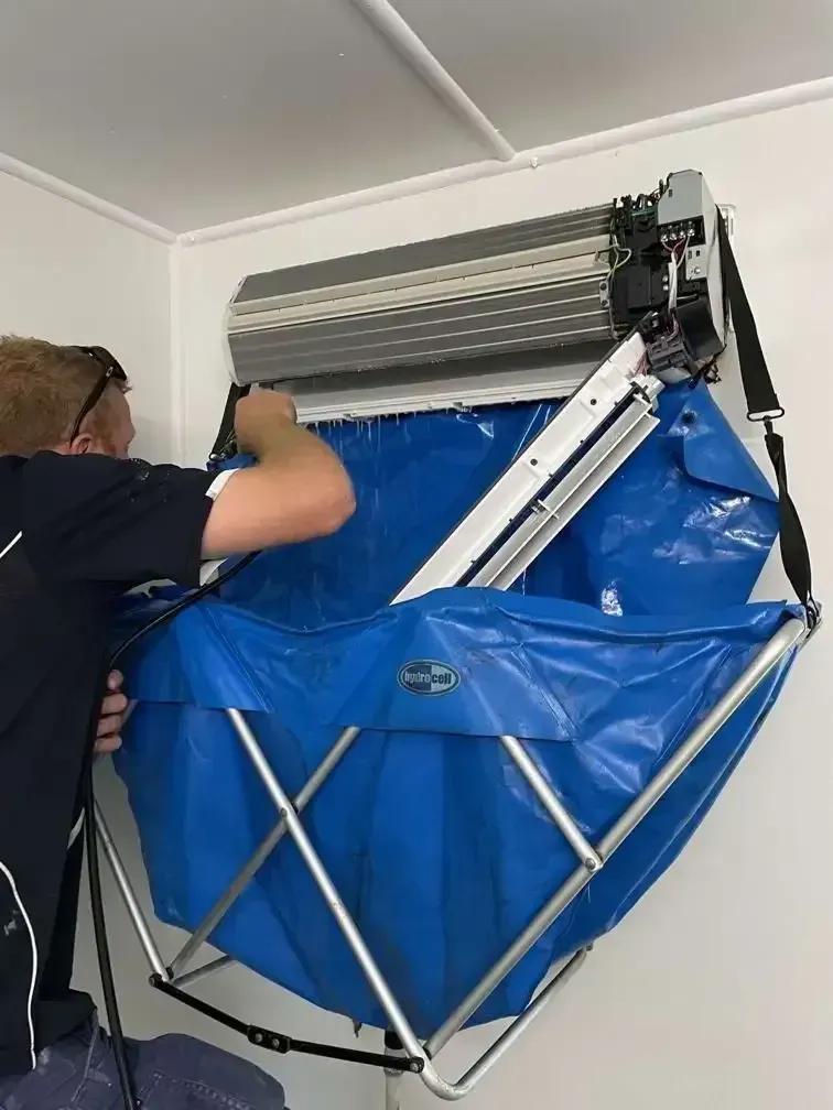 A Man Is Cleaning An Air Conditioner With A Blue Bag — Beards Refrigeration & Air Conditioning in Mackay, QLD