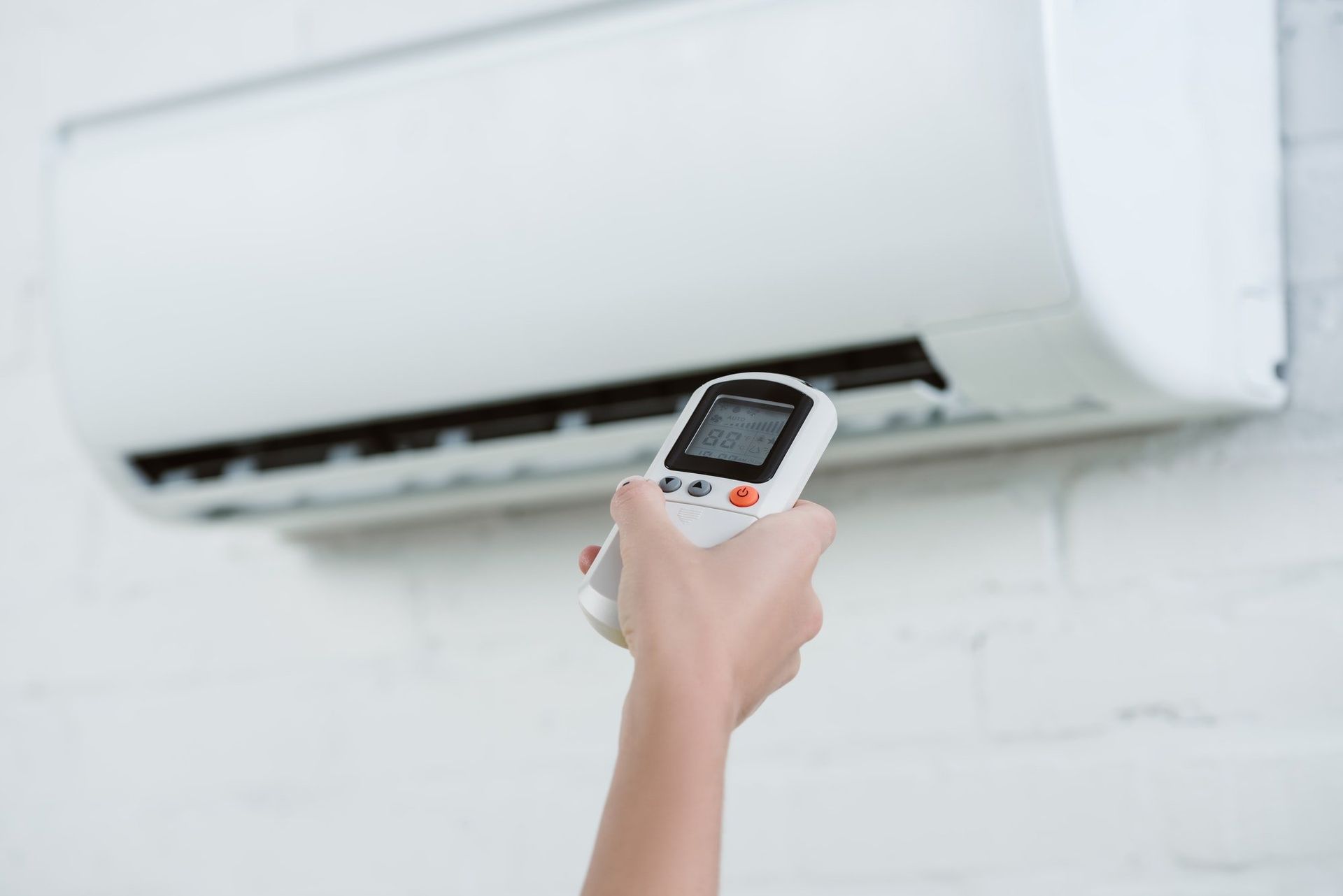 A Person Is Holding A Remote Control In Front Of An Air Conditioner — Beards Refrigeration & Air Conditioning in Marian, QLD