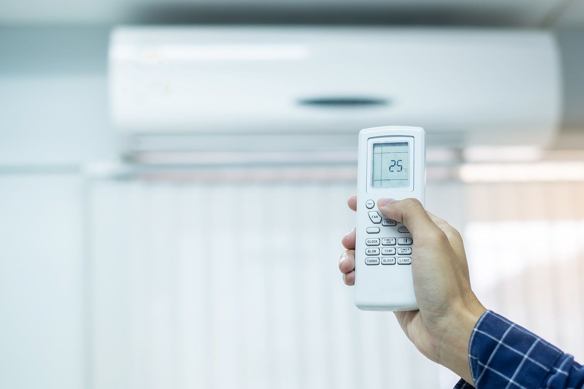 A Person Is Holding A Remote Control In Front Of An Air Conditioner — Beards Refrigeration & Air Conditioning in Sarina, QLD
