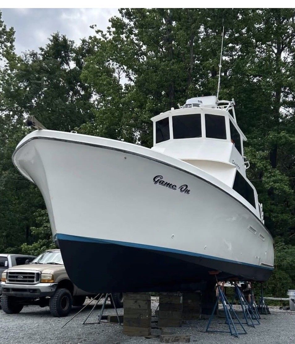 Large white and blue boat on stands in a parking lot with trees in the background