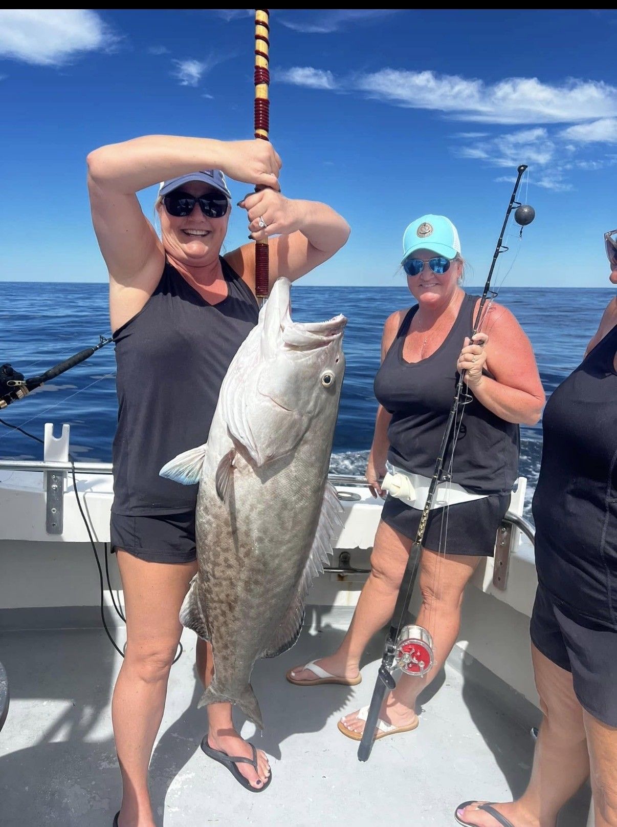Two anglers on a boat holding large fish, with ocean and blue sky in the background.