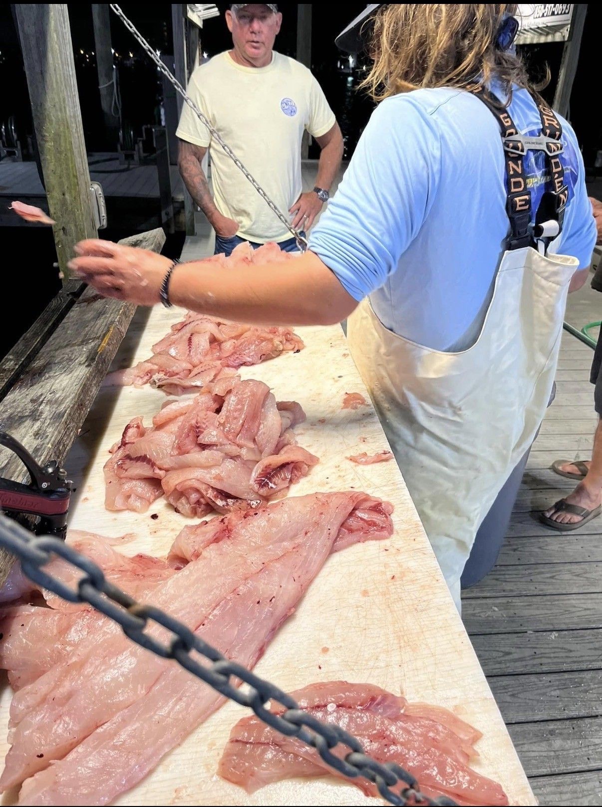 Workers handling piles of raw fish on a table at an outdoor dockside market