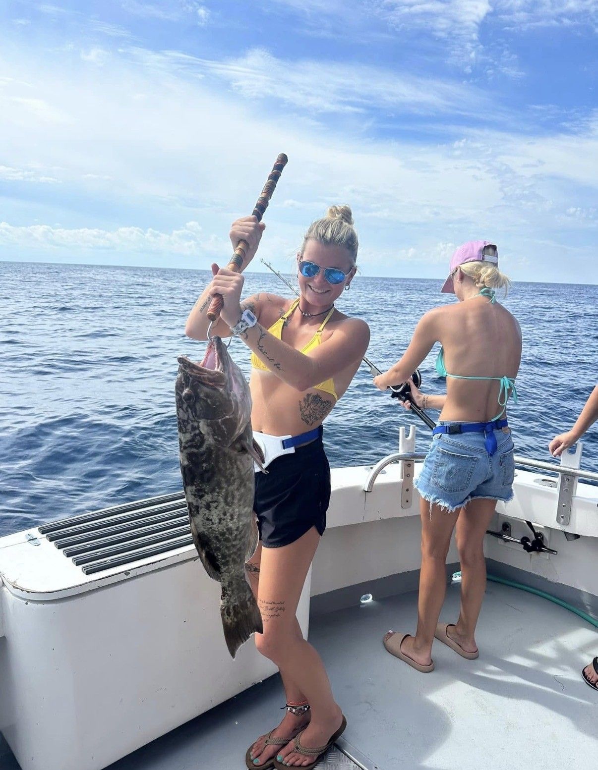 Person on a boat holds up a large fish over the ocean, with two others fishing nearby.