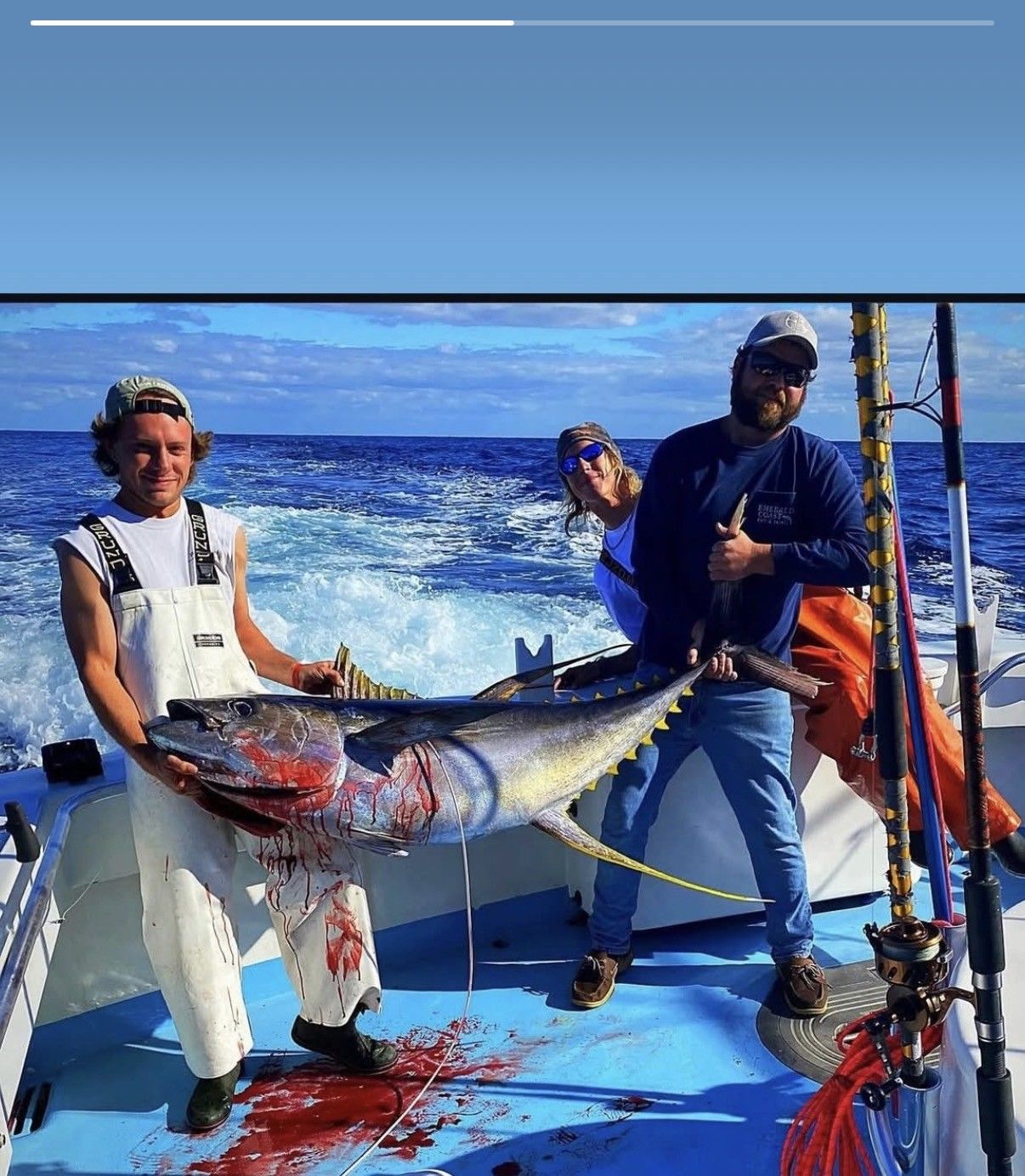 Two anglers on a boat hold a large red-and-silver fish with blood on the deck and ocean behind them