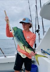 Person on a boat holding a large green-yellow fish by the gills.
