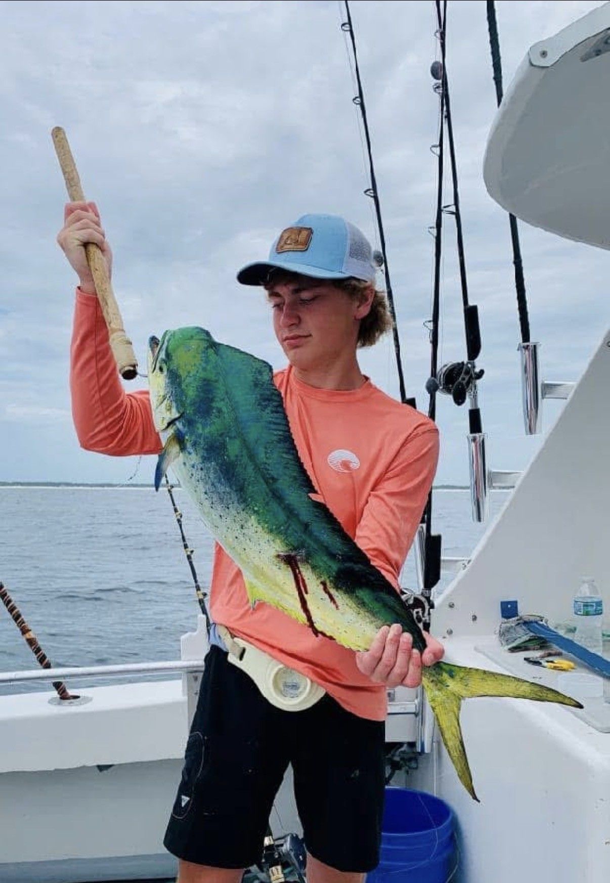 Person on a boat holding a large green-yellow fish by the tail and body, ocean in background