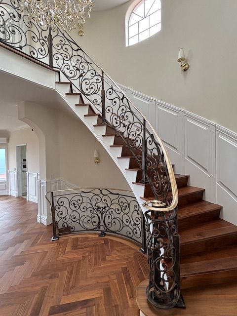 Elegant staircase with ornate wrought-iron railing, wooden steps, and a curved design.