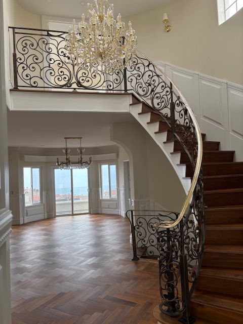Grand foyer with ornate wrought-iron railing, wooden staircase, and chandelier.