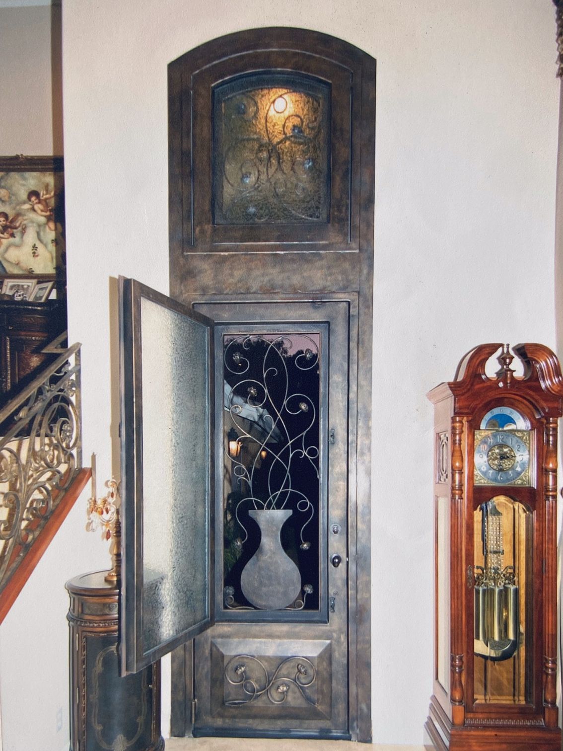 Ornate entryway with open door, frosted glass, and decorative ironwork. Grandfather clock on the right.