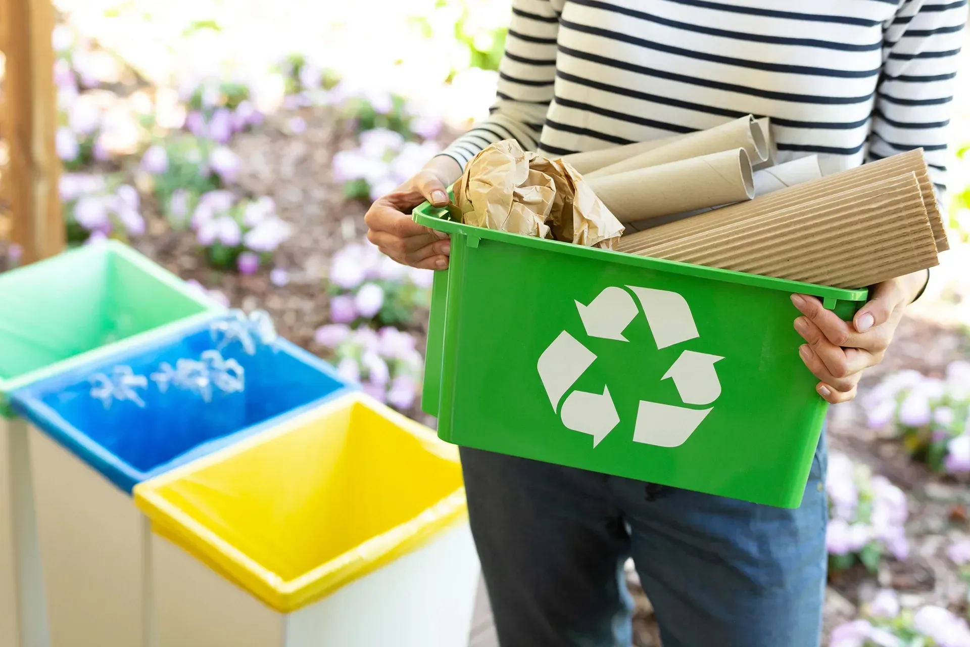 A woman is holding a green recycling bin filled with paper.