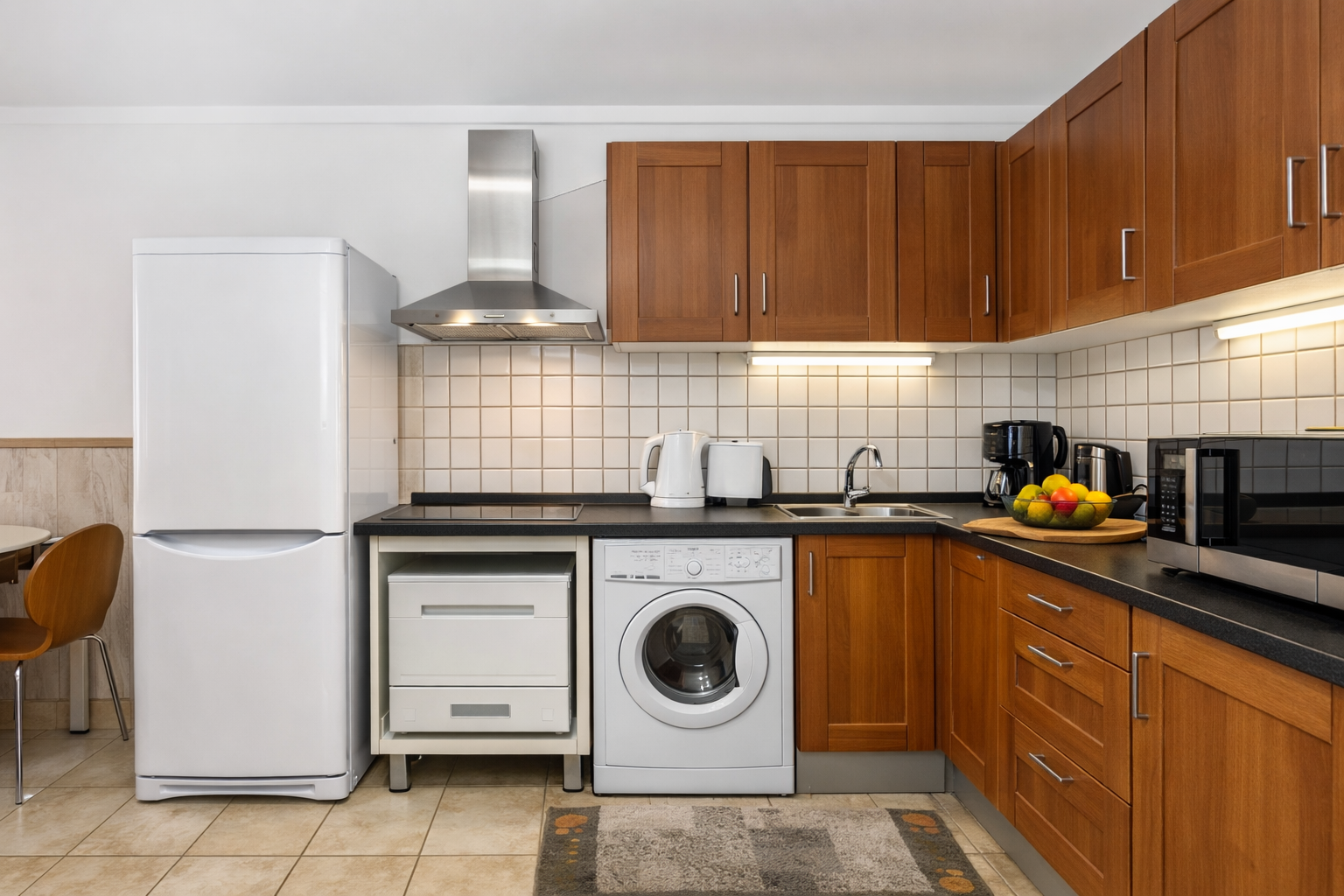 A kitchen featuring wooden cabinets, a white refrigerator, a washing machine, a stove hood, and a microwave on a dark top.