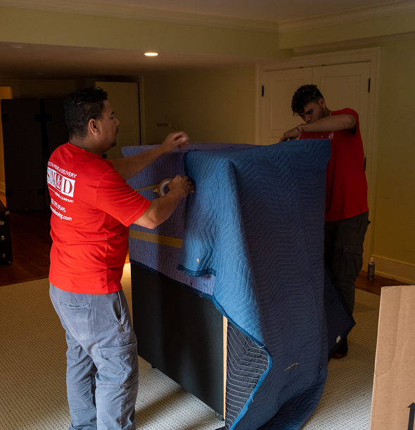 Two Smooth Move & Delivery specialists using protective blankets to wrap a large specialty item for a move in Norwalk.