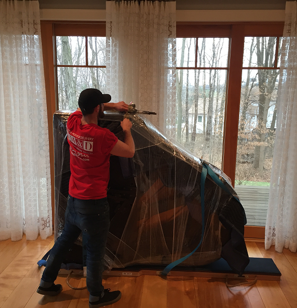 Smooth Move & Delivery specialist in Norwalk expertly wrapping a grand piano for safe transport using professional moving stretch wrap.