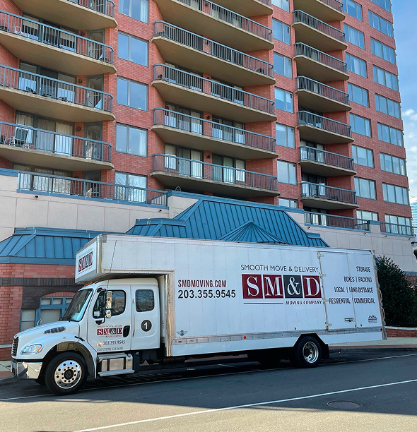 Moving truck parked in front of a tall brick apartment building.