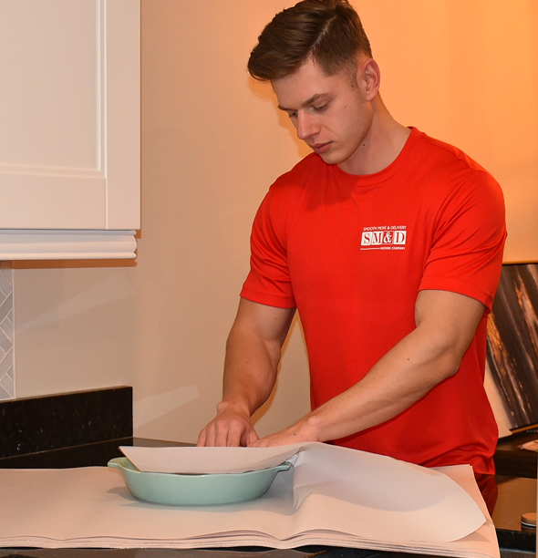 Man in a red shirt placing parchment paper in a teal baking dish on a counter.