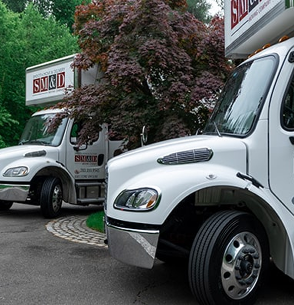 Two white moving trucks parked near a tree, logo visible: SM&J.