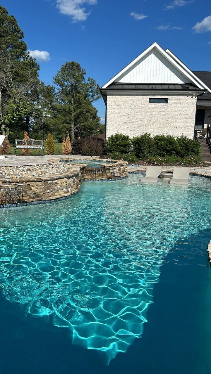 Backyard pool with turquoise water beside a stone spa and beige house under a blue sky