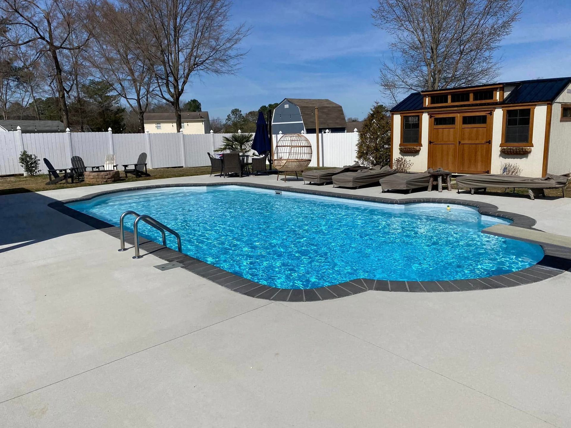 Backyard swimming pool with bright blue water, concrete deck, and a small pool house under a clear sky