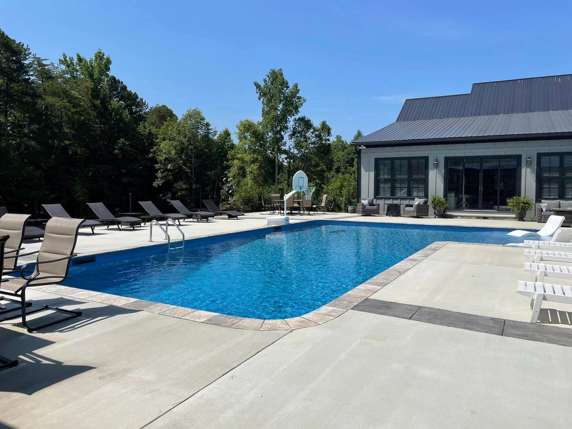 Outdoor swimming pool with lounge chairs beside a modern building under a clear blue sky
