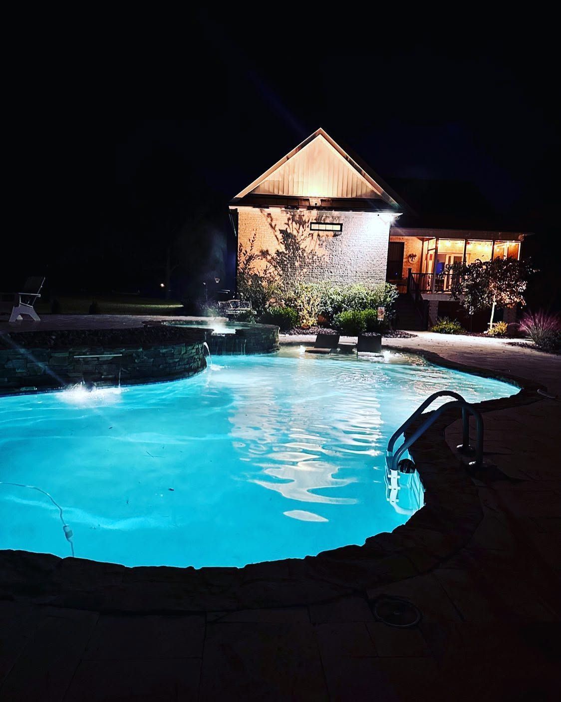 Nighttime pool illuminated blue beside a lit cottage and patio.