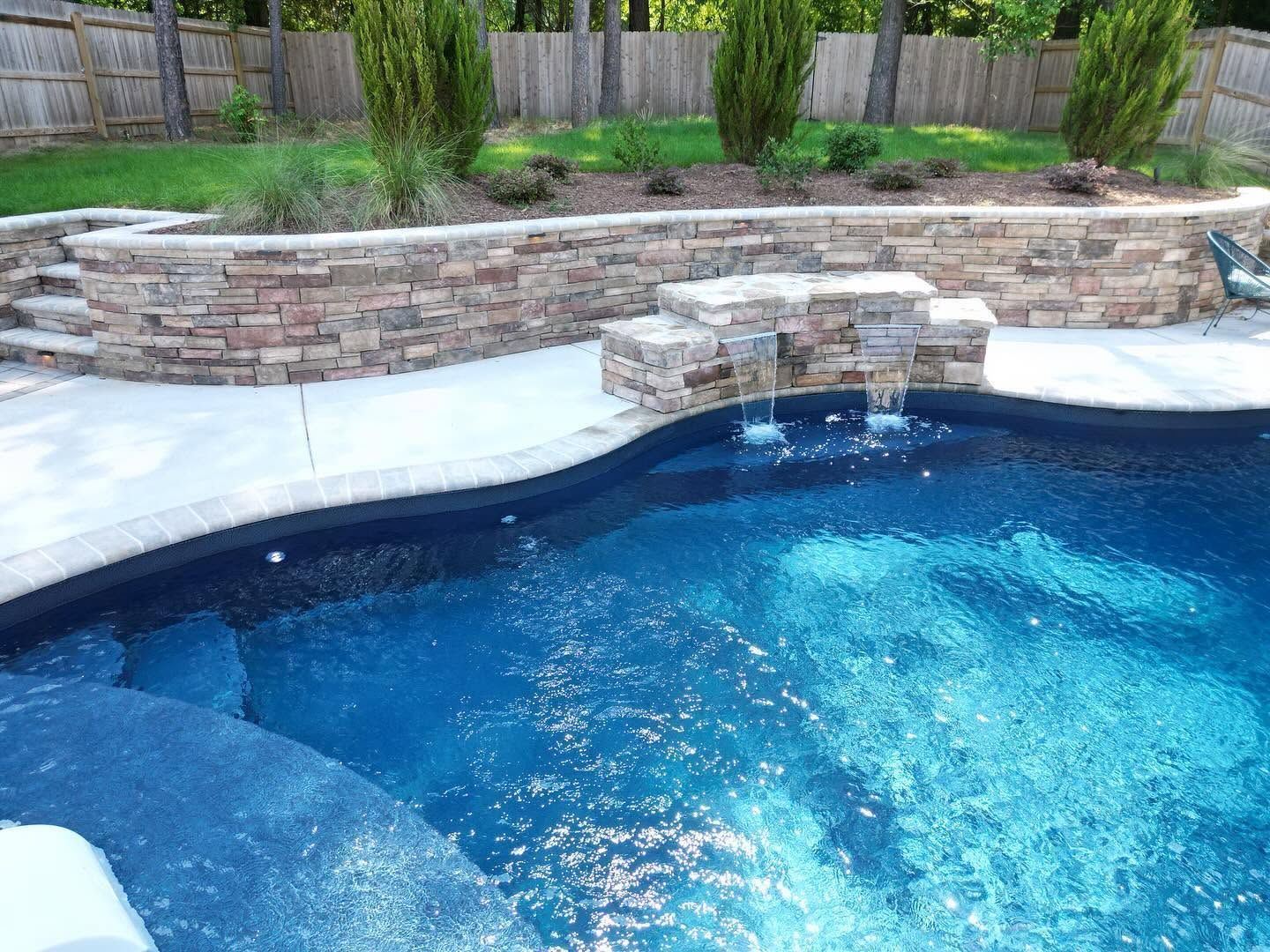 Backyard swimming pool with blue water and a stone waterfall wall