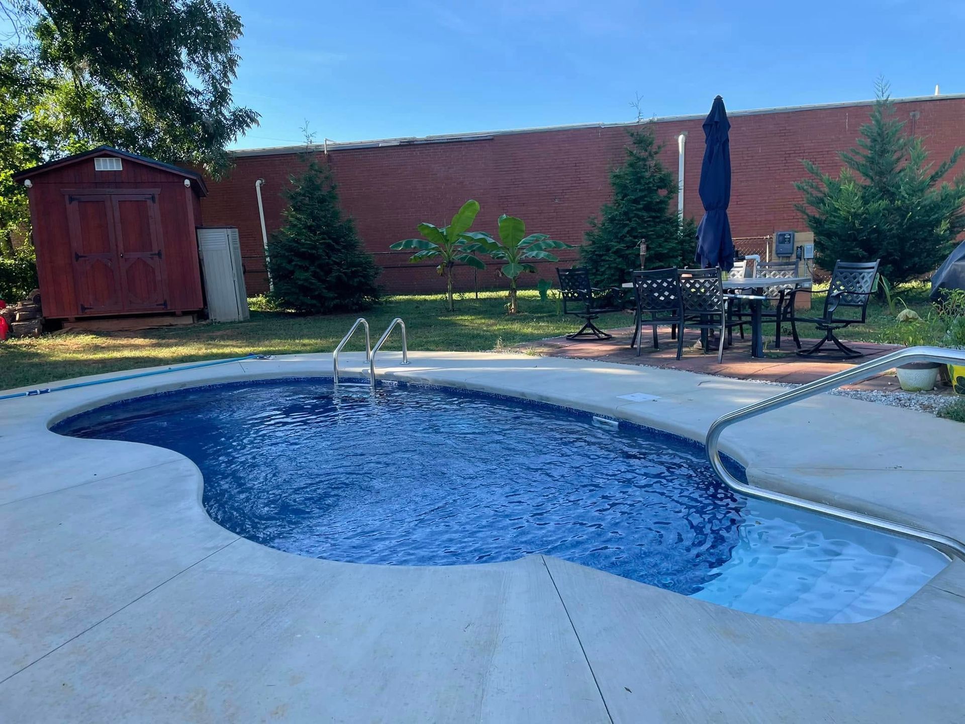 Backyard pool with blue water, patio chairs, and a red shed beside a brick wall