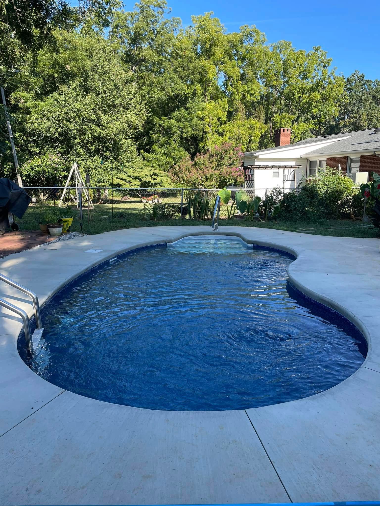 Backyard swimming pool with blue water, curved white deck, and trees in the background