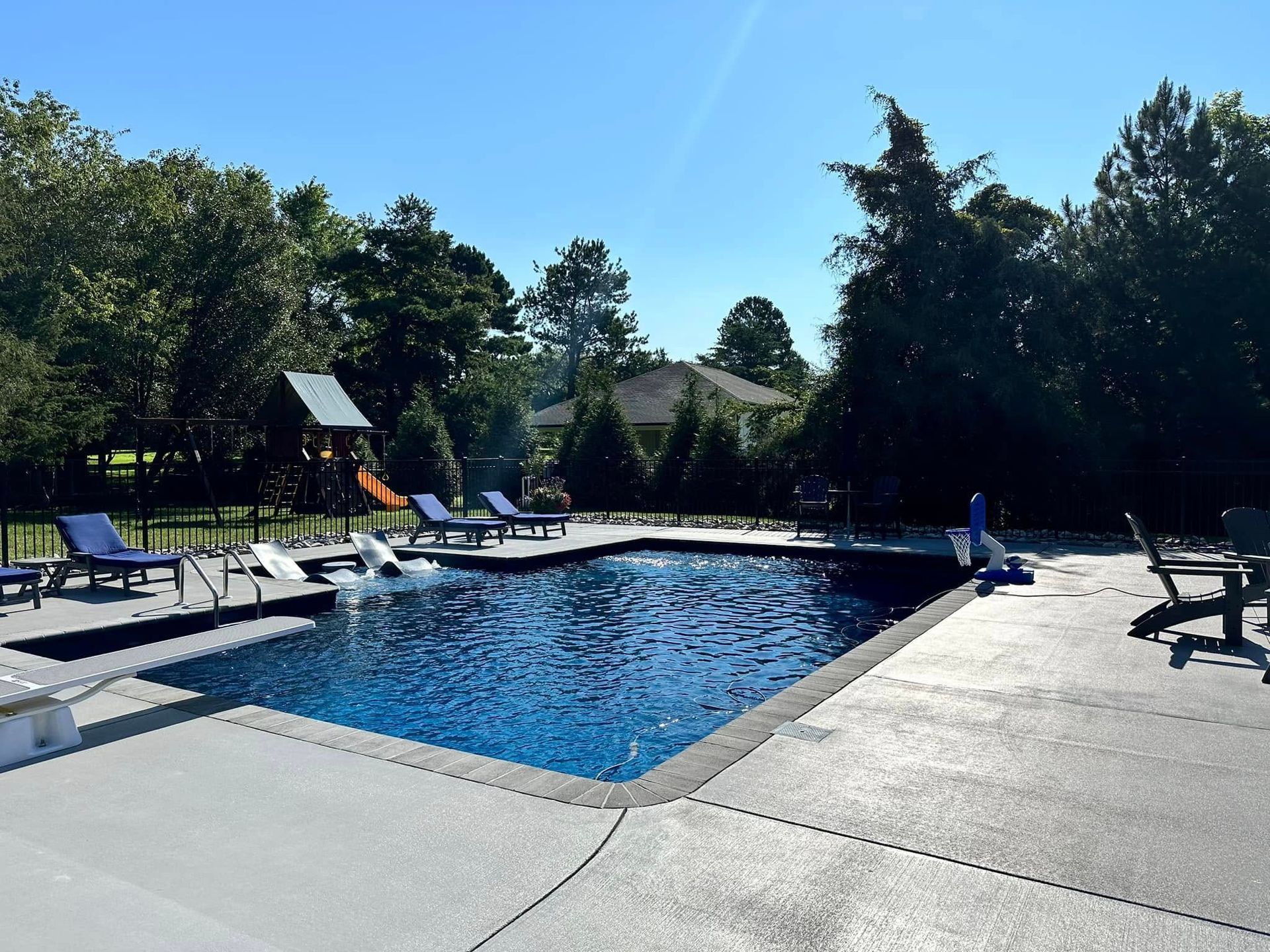 Backyard swimming pool with lounge chairs, patio, and trees under a clear blue sky