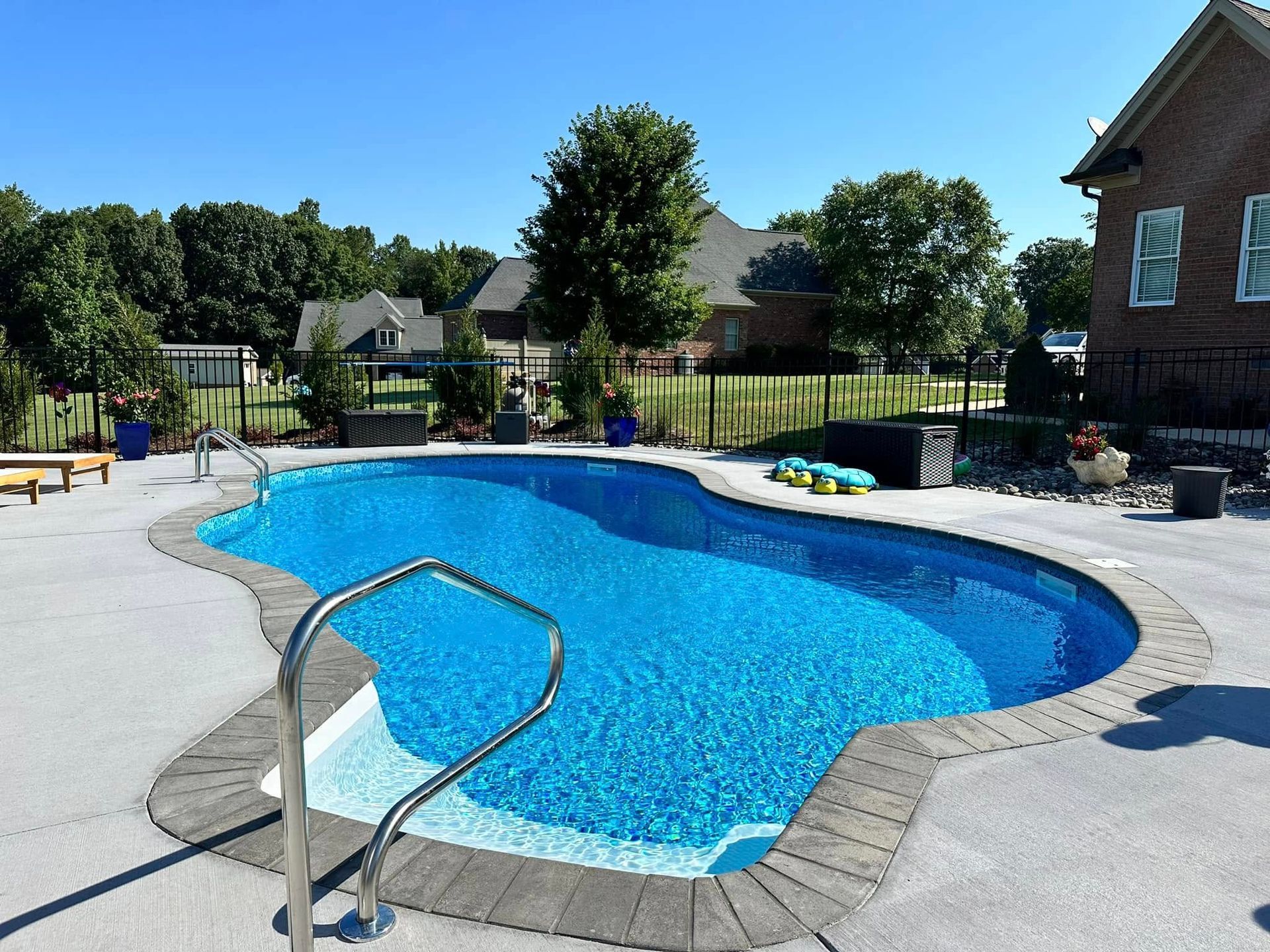 Backyard swimming pool with blue water, concrete deck, and metal handrail under sunny skies