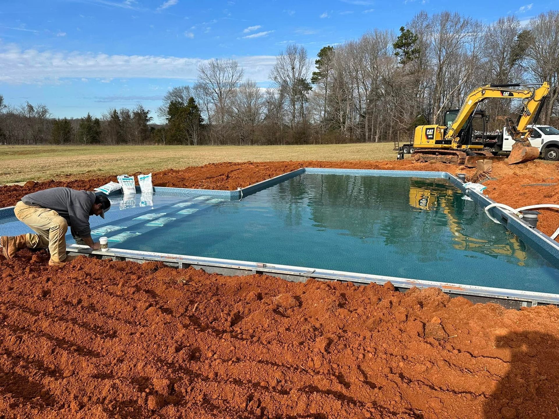Worker leveling water in a pond under construction with excavator nearby