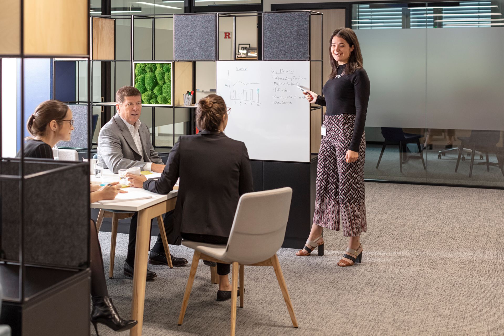 A woman is standing in front of a whiteboard giving a presentation to a group of people.