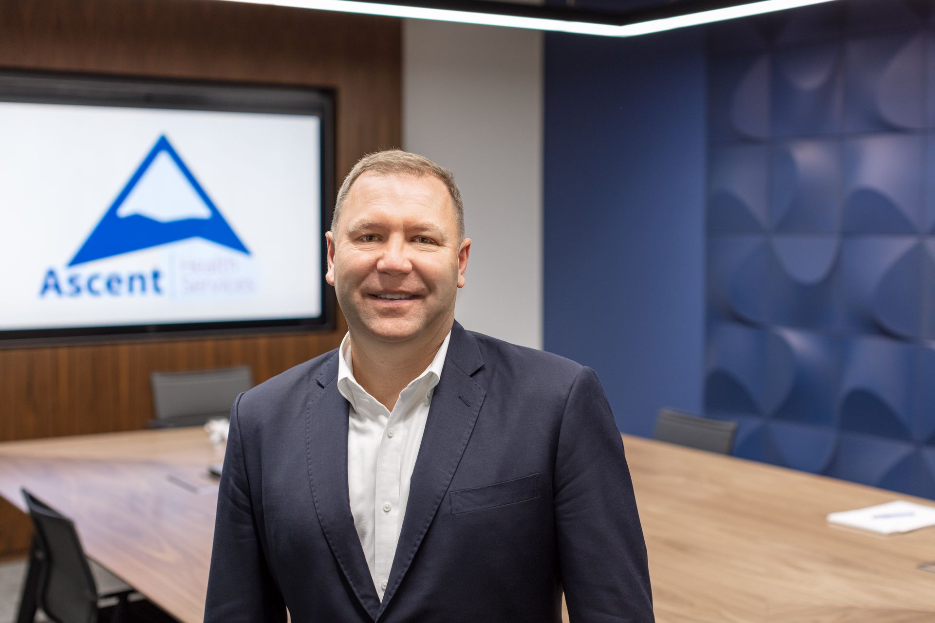 A man in a suit is standing in front of a conference table in a conference room.
