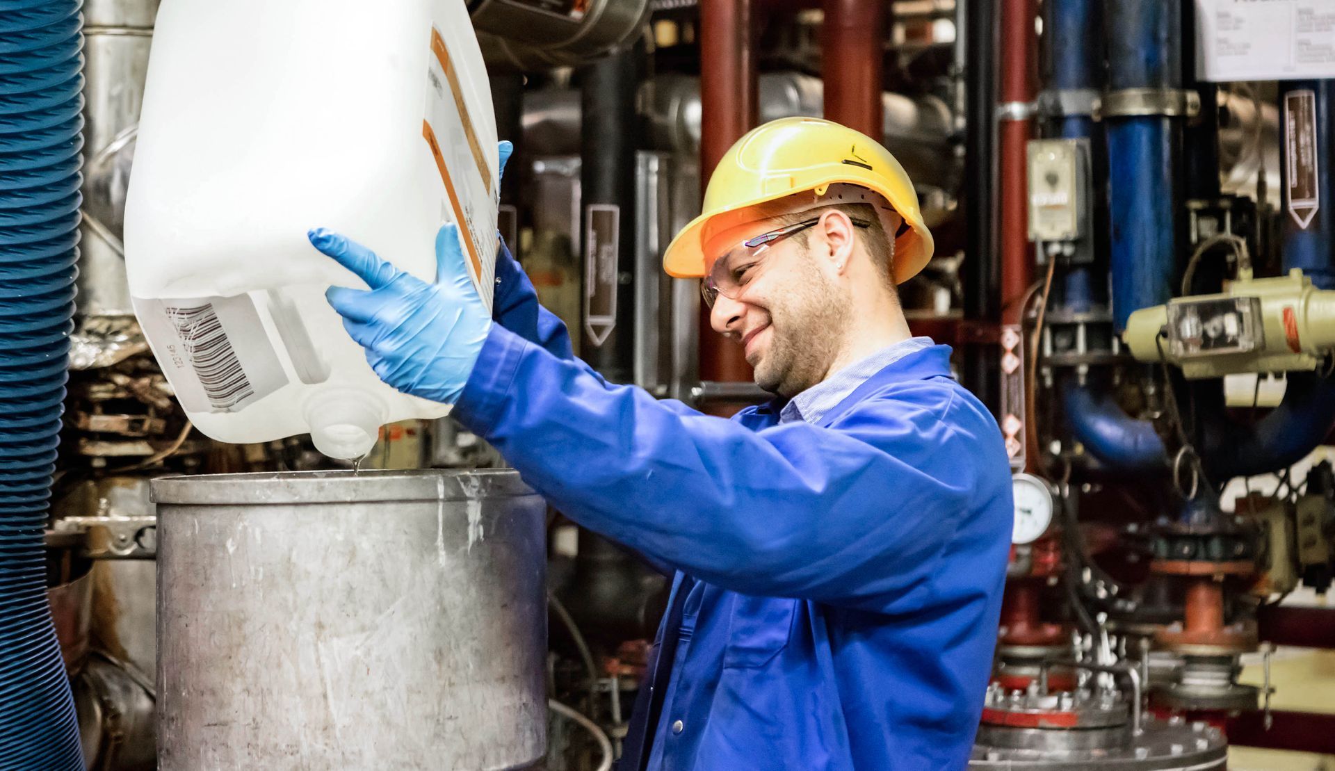 A CONICA worker in a hard hat is pouring liquid into a container in a factory.