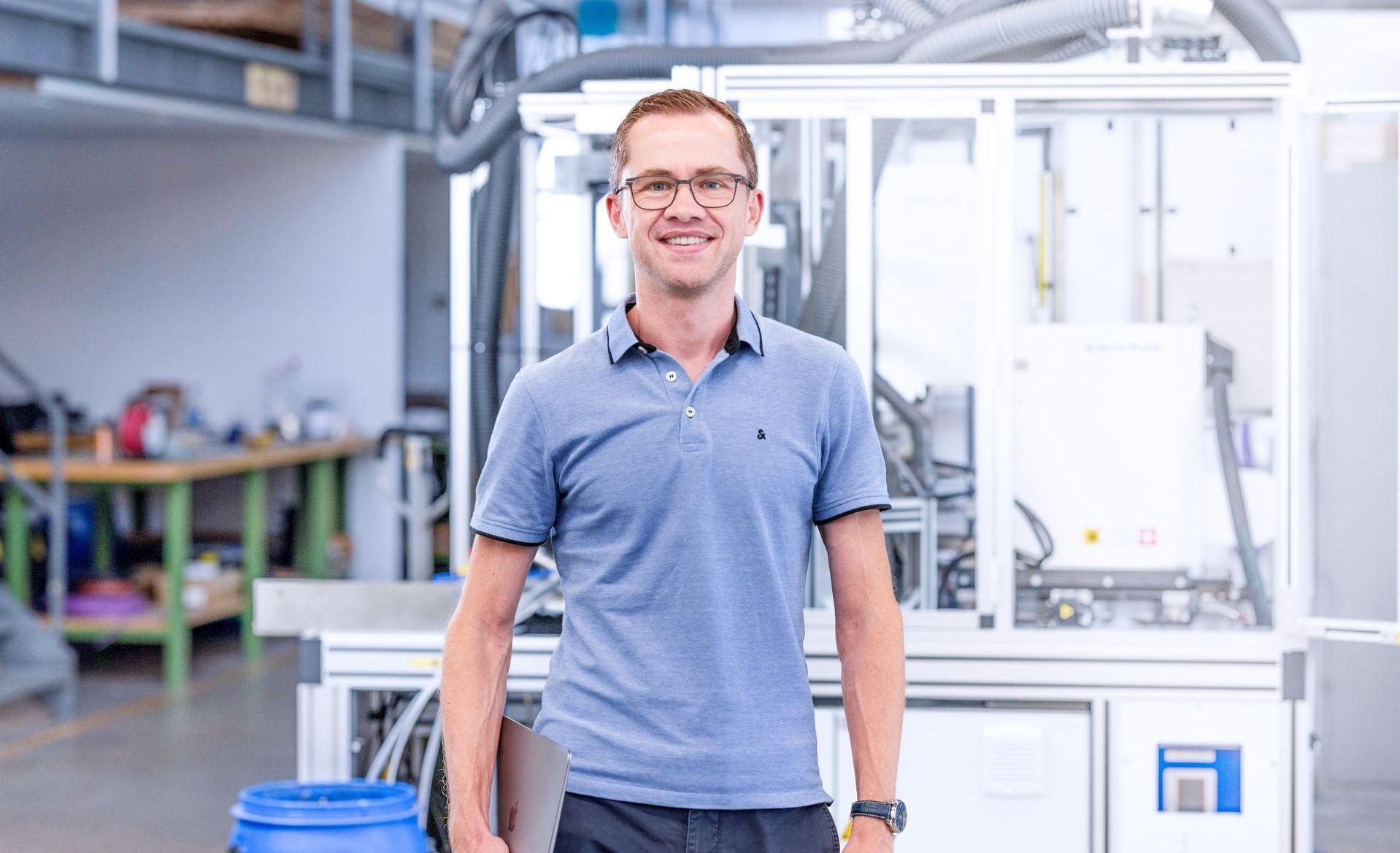 Daniel Fahl, Managing Director of Teca-Print steht vor einer Maschine in einer Fabrik in einem blauen Polo-Shirt.