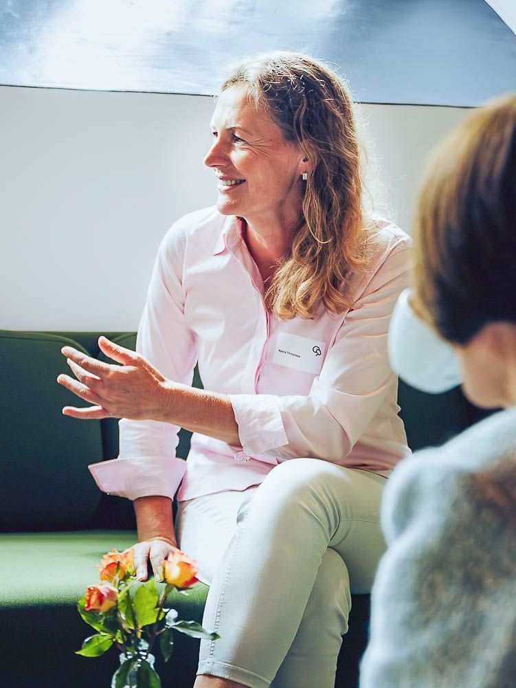 A woman in a pink shirt is sitting on a green couch talking to another woman.