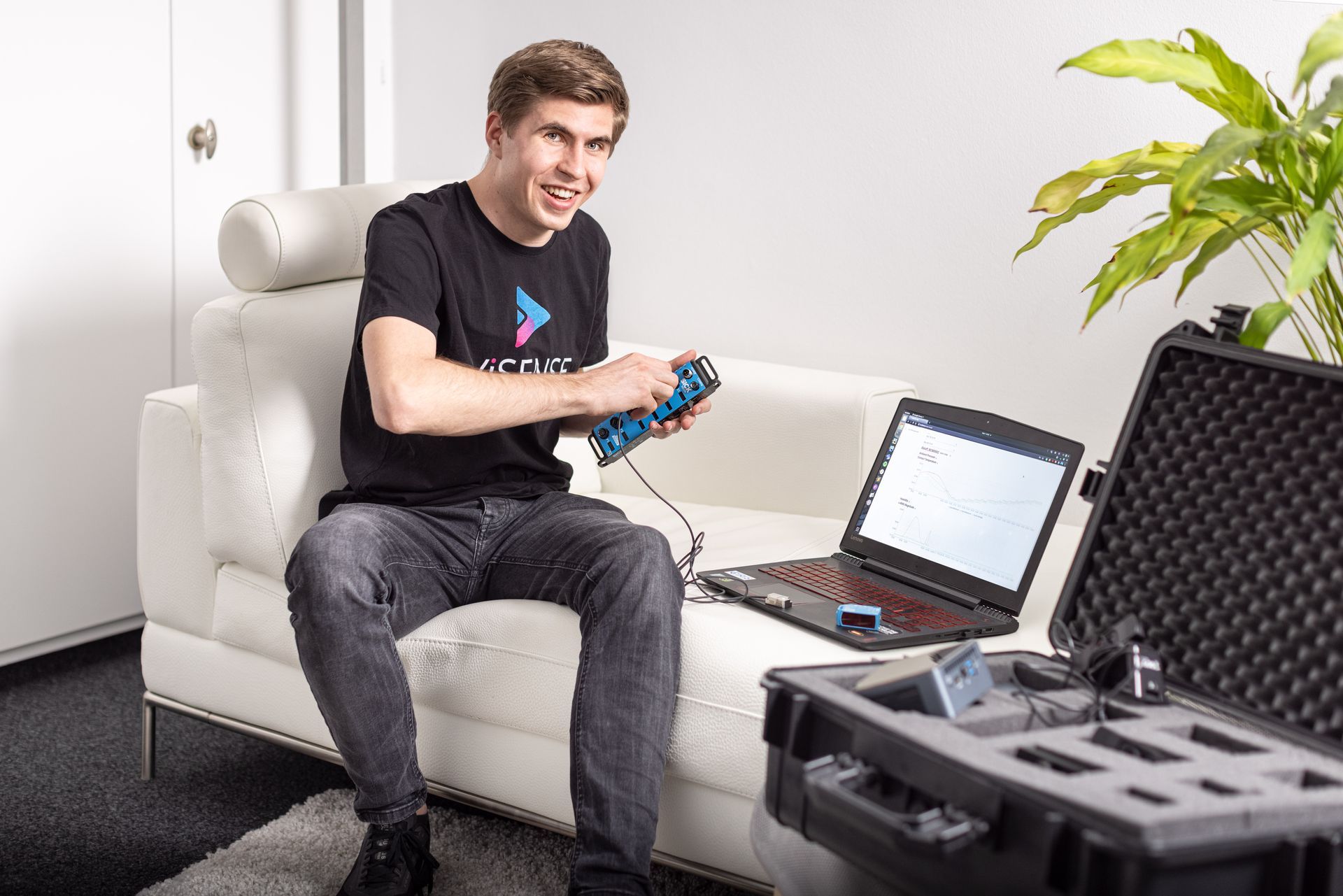 A man is sitting on a couch with a laptop and a remote control.