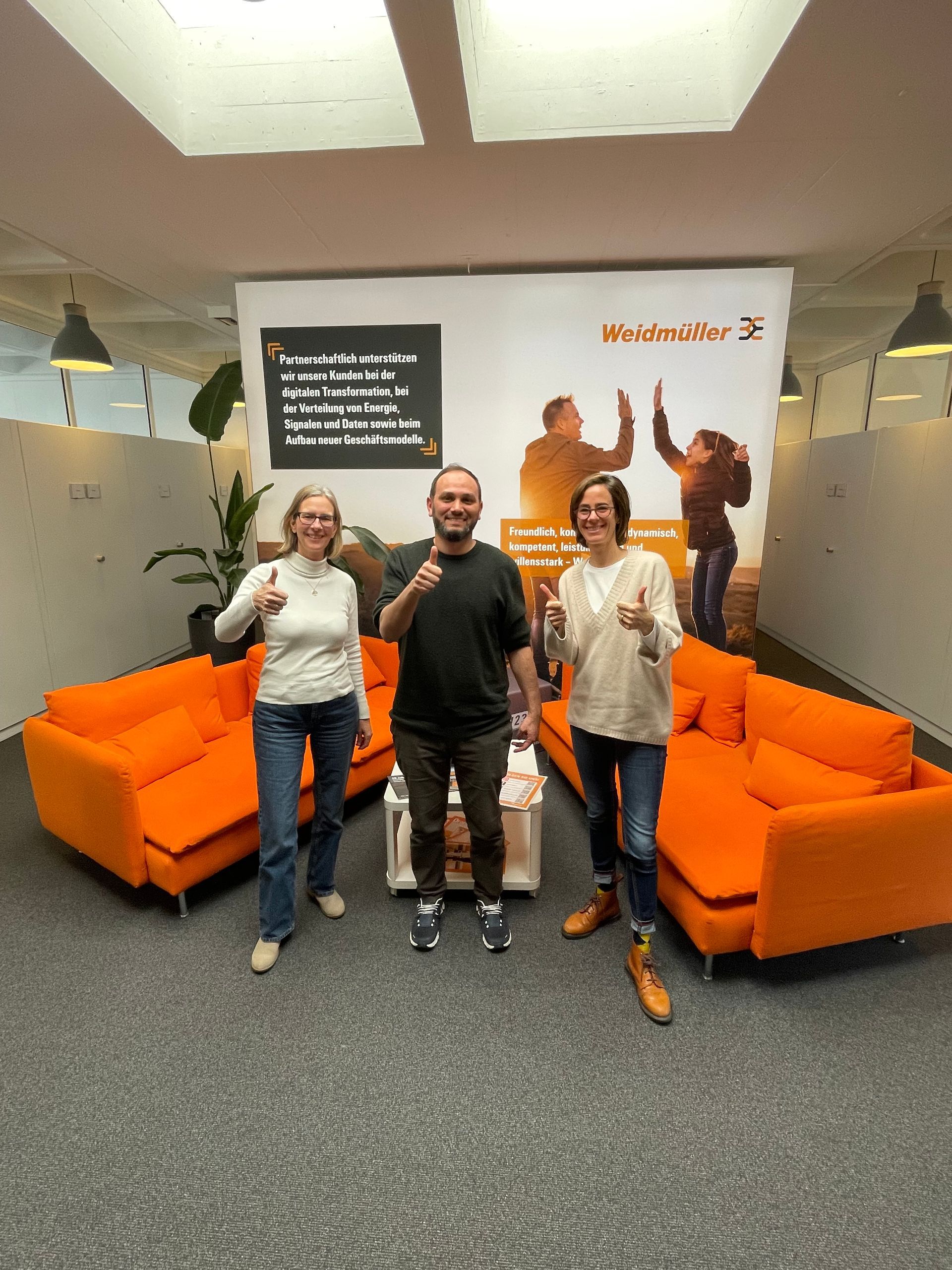 Eine Gruppe von Menschen posiert für ein Foto in einem Raum mit orangefarbenen Sofas.