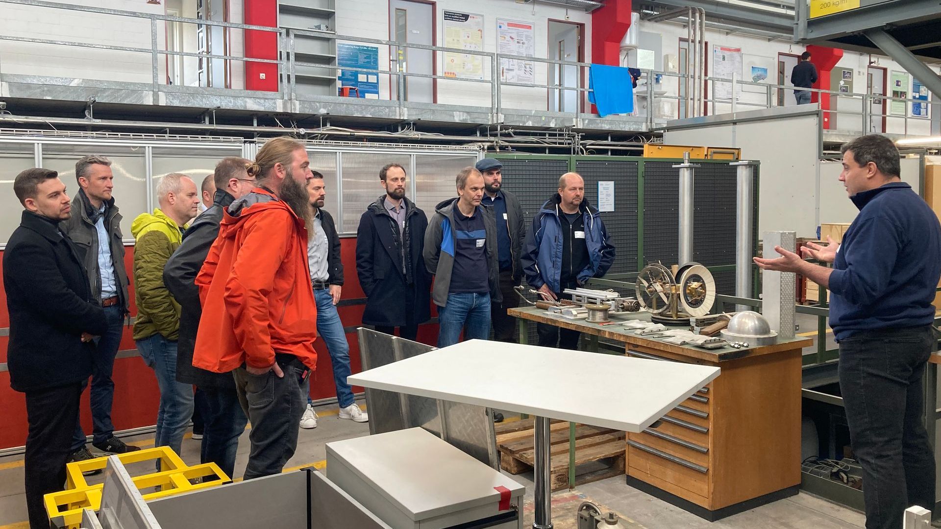 Eine Gruppe von Männern steht in einer Fabrik um einen Tisch herum.