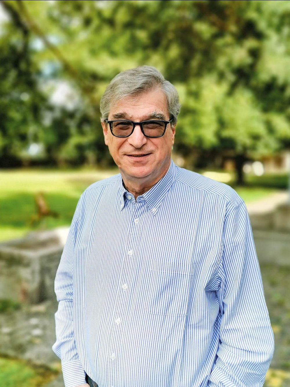 Ein Mann mit Brille und gestreiftem Hemd steht in einem Park.